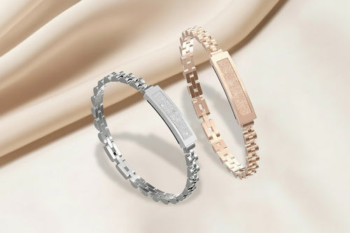 Two smart bracelets, one silver and one rose gold, on a beige fabric background.